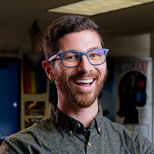 Riley wearing blue framed glasses and smiling