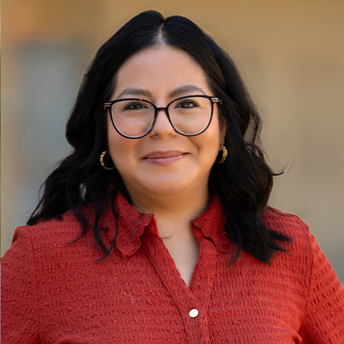 Professional headshot of a person wearing glasses and a red blouse, looking at the camera against a softly blurred background.